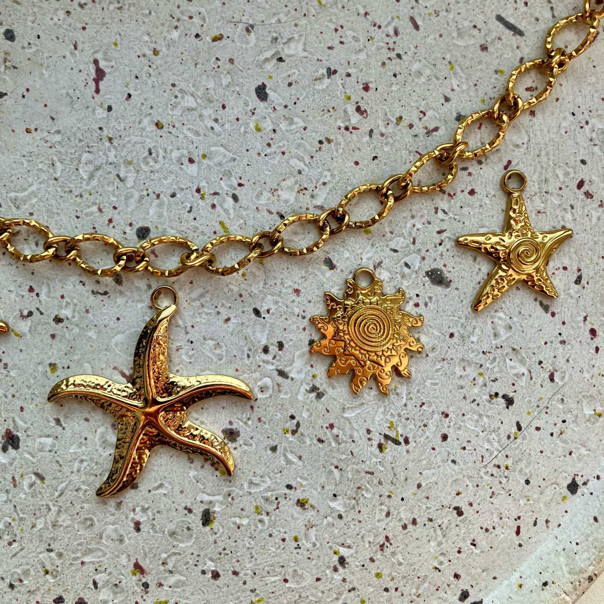 Close-up van drie gouden bedels: een grote zeester, een zon en een kleine gedetailleerde zeester met een spiraalvormig detail in het midden.