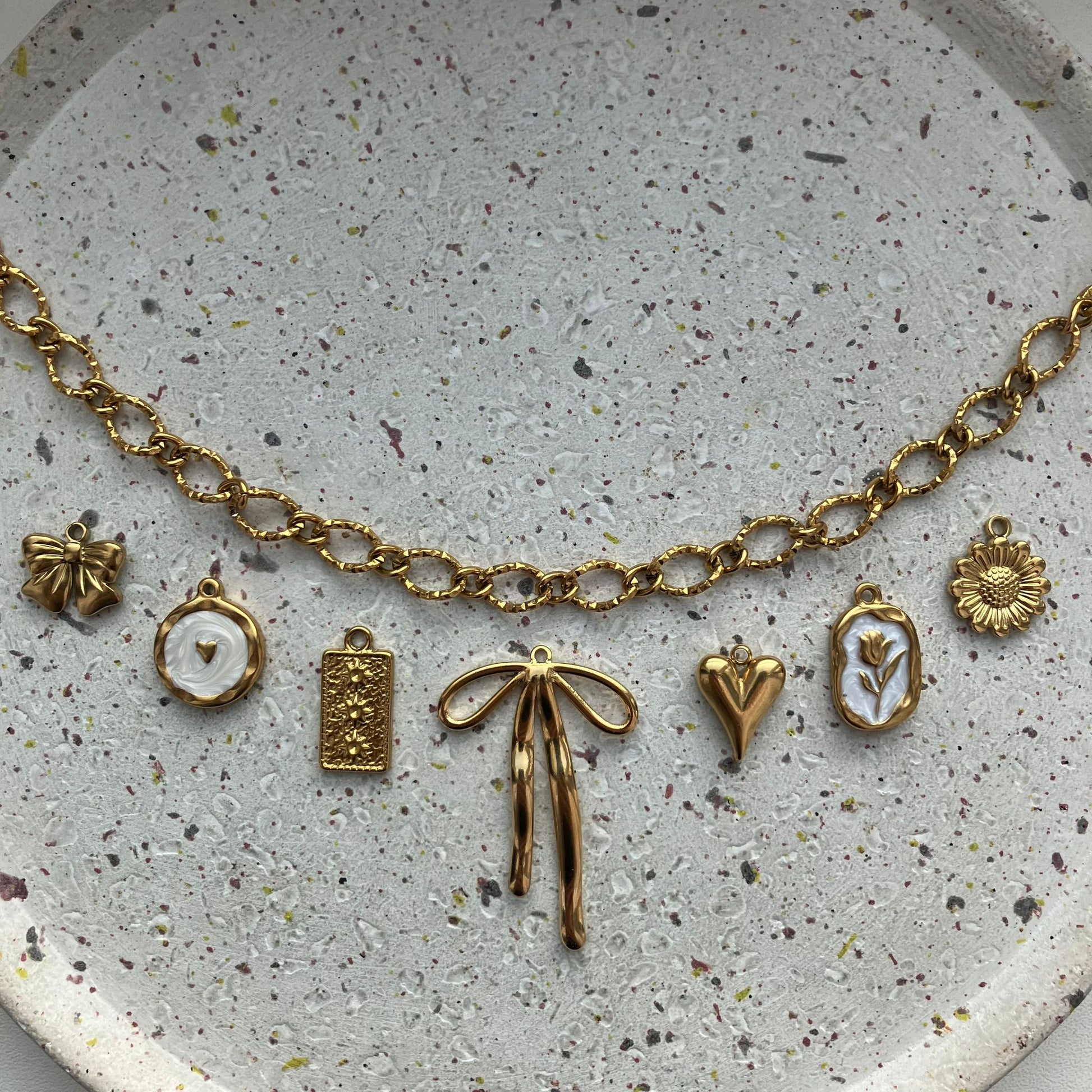 Close-up van gouden bedelketting met strikje, witte bedel met hartje, reliëfbedel, grote strik, hartje, roosbedel en zonnebloem | Zafia Jewellery