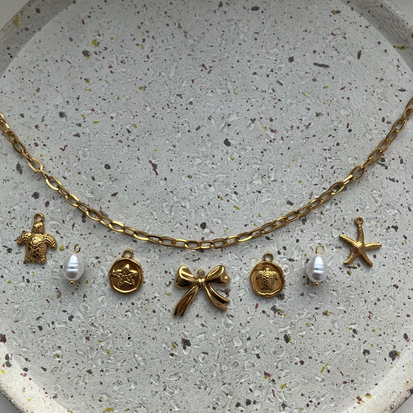 Gouden bedelketting met schakel en 7 bedels: schildpad, parel, ster, strik, schildpad, parel en zeester | Zafia Jewellery