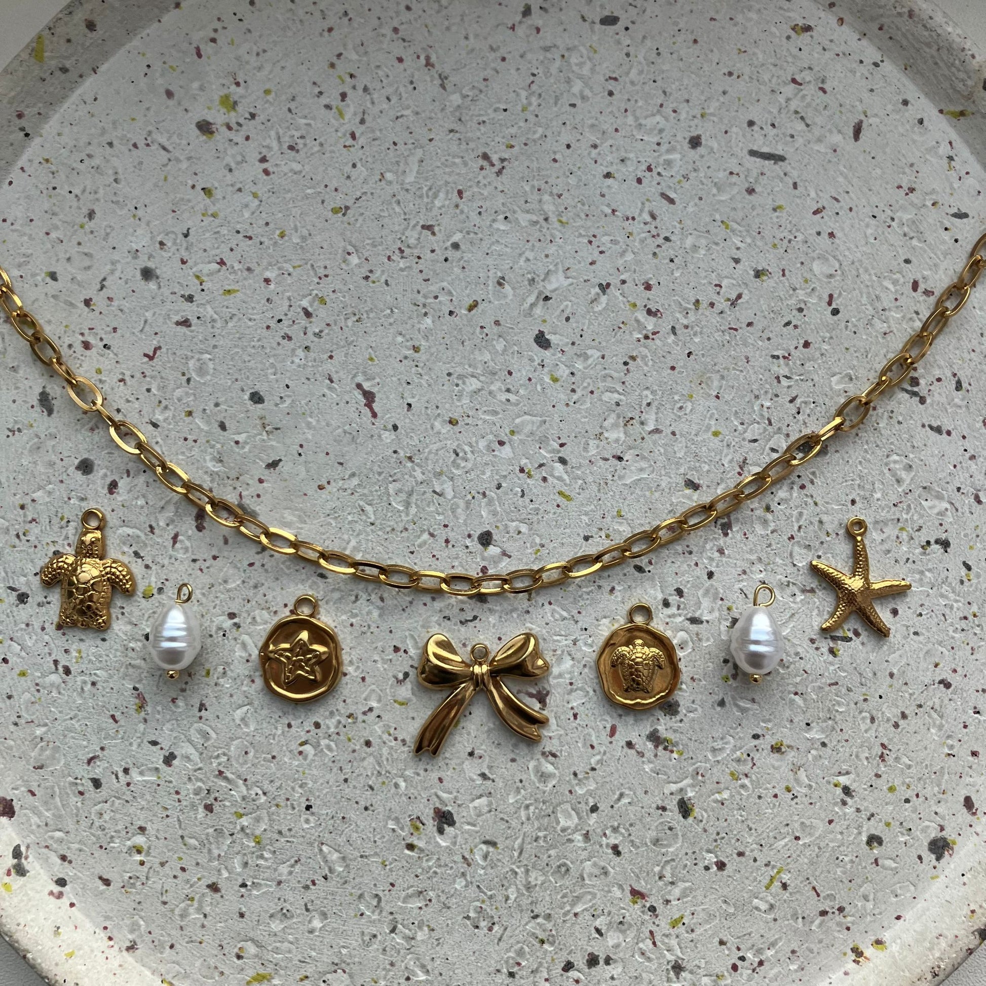 Gouden bedelketting met schakel en 7 bedels: schildpad, parel, ster, strik, schildpad, parel en zeester | Zafia Jewellery