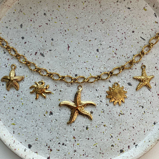 Gouden bedelketting met vijf bedels van links naar rechts: een zeester met details, een zon, een grote zeester, een zon met veel details en een gedetailleerde zeester.