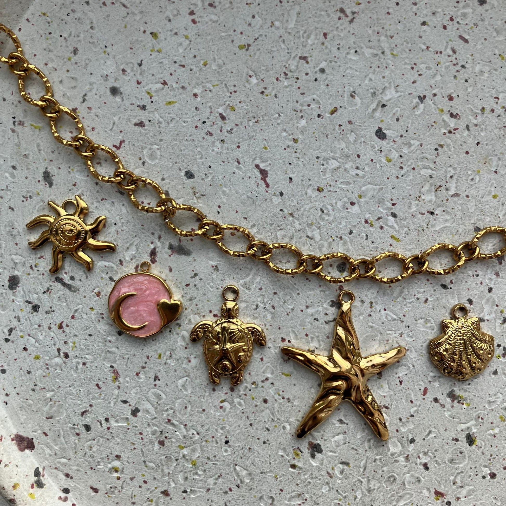 Close-up van bedels, van links naar rechts: een zon, een roze cirkel met een man erin, een schattige schildpad, een grote zeester en een schelp | Zafia Jewellery