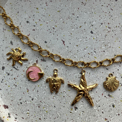Close-up van bedels, van links naar rechts: een zon, een roze cirkel met een man erin, een schattige schildpad, een grote zeester en een schelp | Zafia Jewellery
