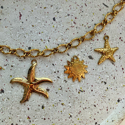 Close-up van drie gouden bedels: een grote zeester, een zon en een kleine gedetailleerde zeester met een spiraalvormig detail in het midden.