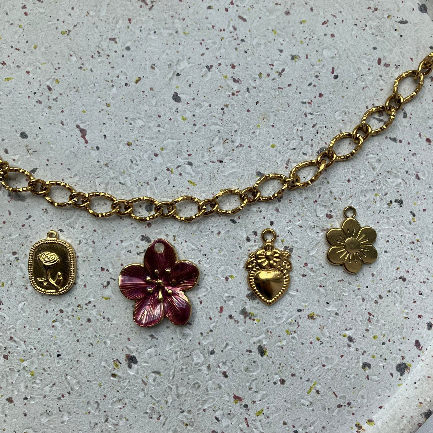 Close-up van een rechthoekige bedel met een roos erin, een bedel in de vorm van een bordeauxrode bloem, een bedel in de vorm van een hartje met een klein bloemetje erop, en een extra kleine bloemetjebedel ernaast | Zafia Jewellery