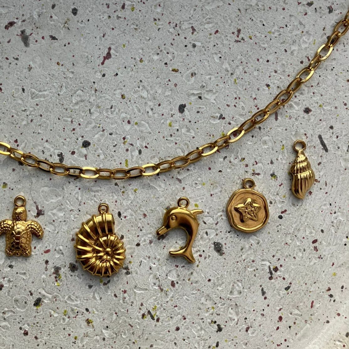 Detailfoto van een gouden bedelketting met schelp, dolfijn, bloemetje en extra schelpbedel – Zafia Jewellery