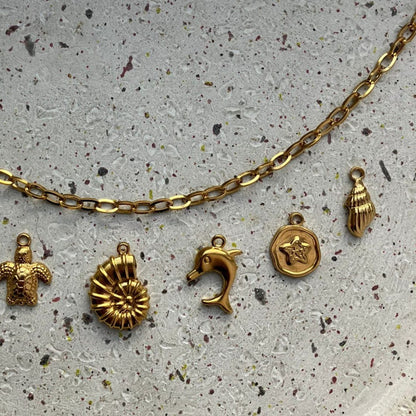 Detailfoto van een gouden bedelketting met schelp, dolfijn, bloemetje en extra schelpbedel – Zafia Jewellery