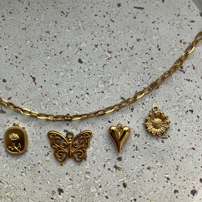 Close-up van vier gouden bedels: roosgravure, vlinder, klassiek hartje en zonnebloem met reliëf | Zafia Jewellery