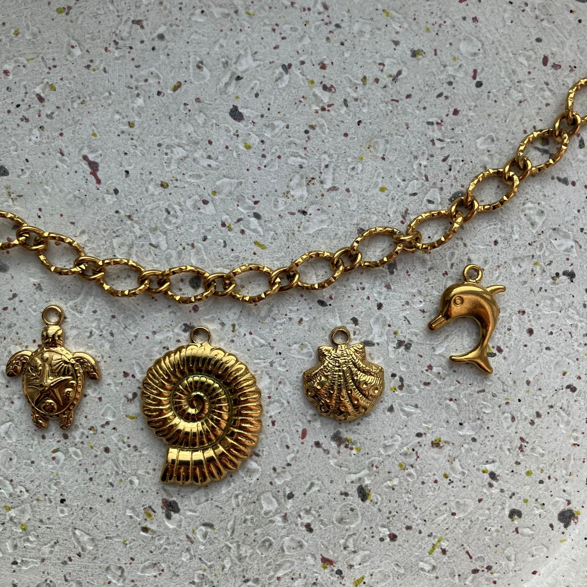 Close-up van vier gouden bedels: schildpad, spiraalvormige ammoniet, schelp en speels dolfijntje | Zafia Jewellery