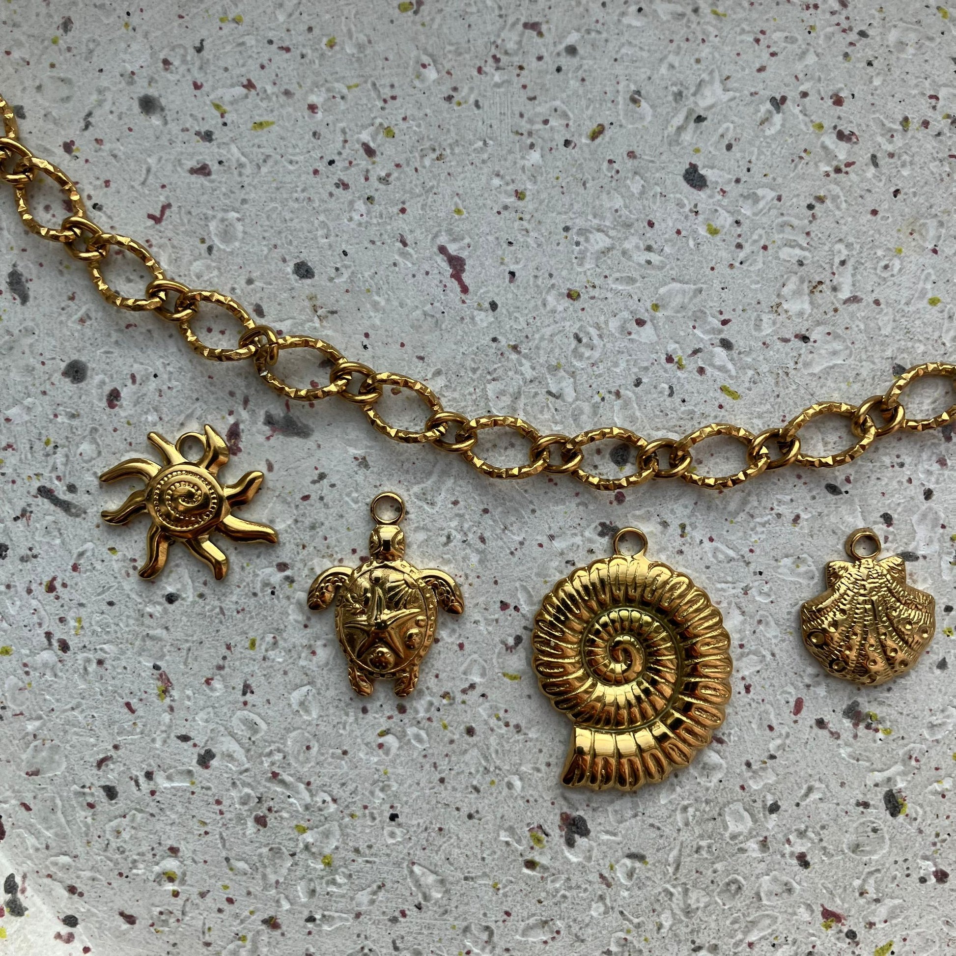 Close-up van vier gouden bedels: zon, schildpad, spiraalvormige ammoniet en fijne schelp | Zafia Jewellery