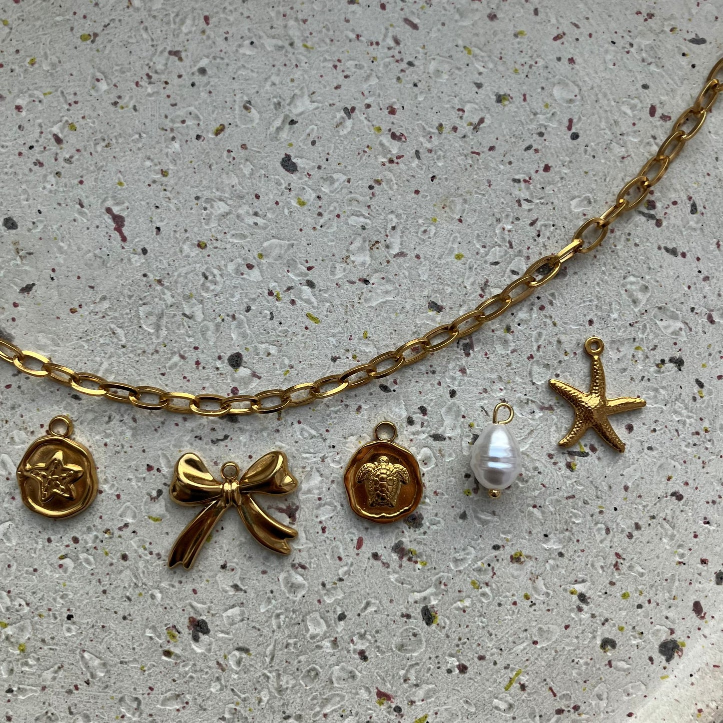 Close-up van vijf bedels: zeesterbedel, strikje, schildpadbedel, witte parel en gedetailleerde zeester | Zafia Jewellery