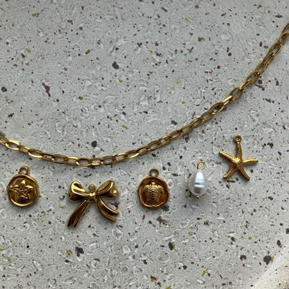 Close-up van vijf bedels: zeesterbedel, strikje, schildpadbedel, witte parel en gedetailleerde zeester | Zafia Jewellery