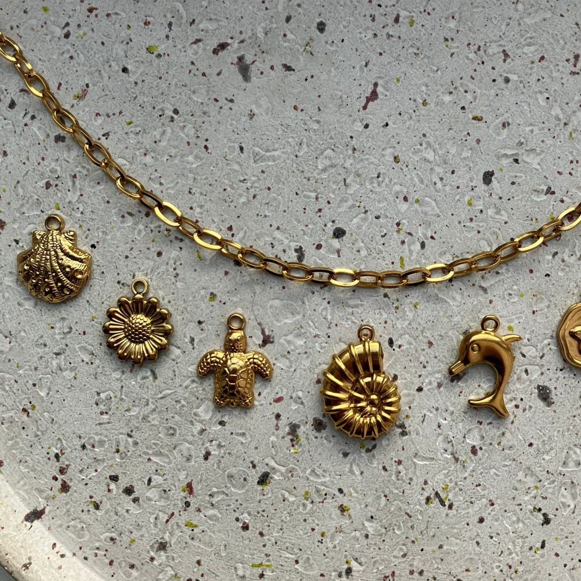 Detailfoto van een zomerse gouden bedelketting met schelpjes, bloem en dolfijn – Zafia Jewellery